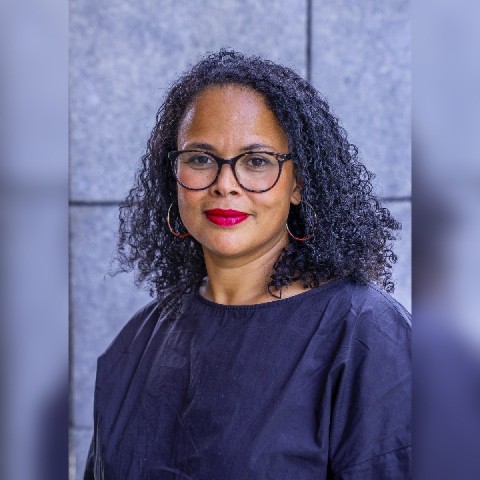 Aileen trägt eine Brille und steht vor einer grauen Wand