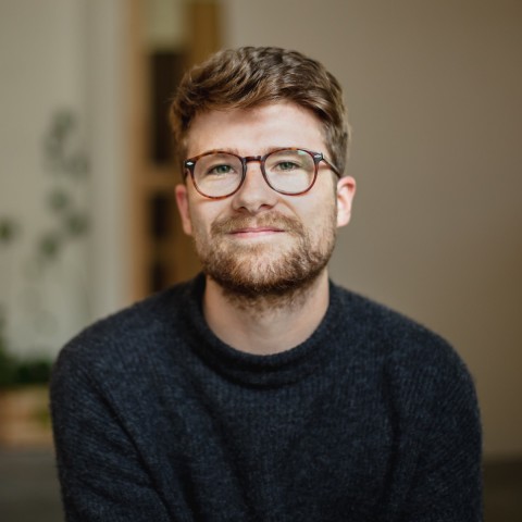 Martin trägt einen Pullover und eine Brille
