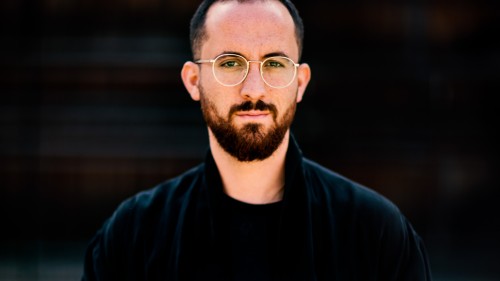 Igor Levit steht in schwarzem Hemd vor einem schwarzen Hintergrund.