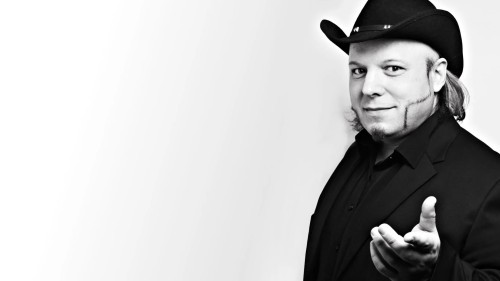 Bruno Kramm trägt einen Cowboyhut und streckt seine geöffnete Hand in Richtung Kamera.
