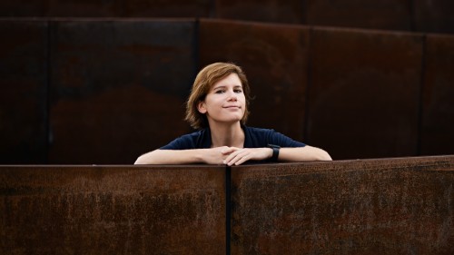 Ingrid Brodnig sitzt zwischen Stuhlreihen und stützt die Unterarme auf die Lehnen. 