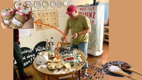 Tisch, Blick von oben auf Utensilien, Topf und Herdplatte, Sascha gibt Senf dazu, Schubladen und Teller an der Wand im HG