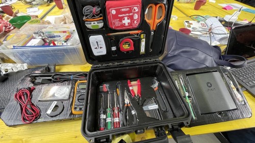 Ein Werkzeugkasten mit Reparatur-Utensilien wie Schraubendrehern und Verbandskasten auf einem großen gelben Tisch voller weiterer Utensilien.