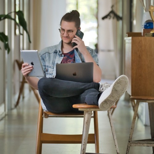 Person sitzt mit verschiedenen technischen Geräten auf einem Stuhl sitzend