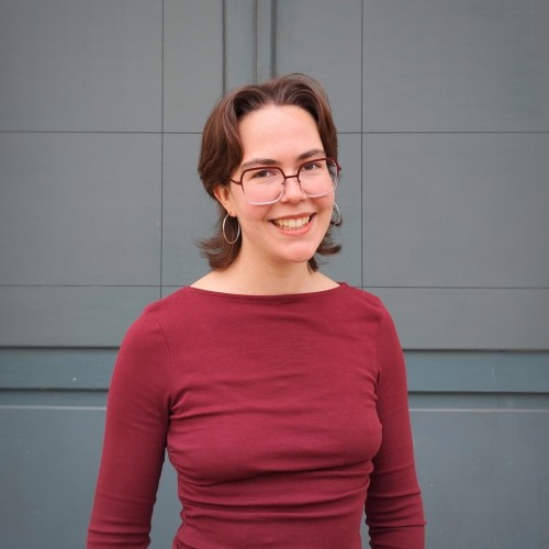 Leonie Heims steht vor einer grauen Fassade und blickt in die Kamera
