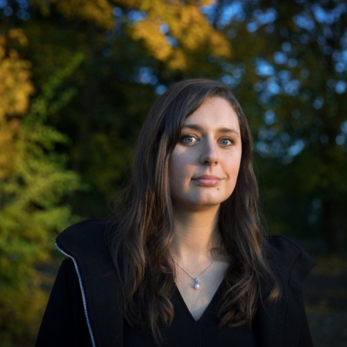 Katharina steht vor einem herbstlichen Wald. 