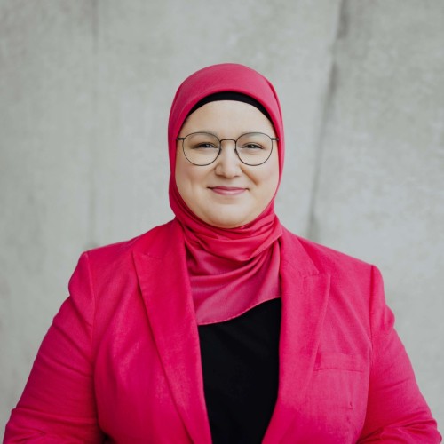 Frontalfoto von Zehra Öztürk vor Betonwand mit pinkem Kopftuch und pinker Jacke