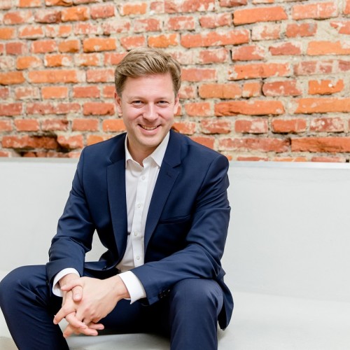 Helge Fuhst sitzt auf einer weißen Bank vor einer Backstein-Wand