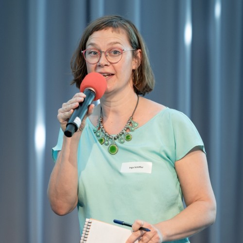 Inga Schiffler spricht in ein rotes Mikro. In der Hand hält sie einen Block und einen Stift.