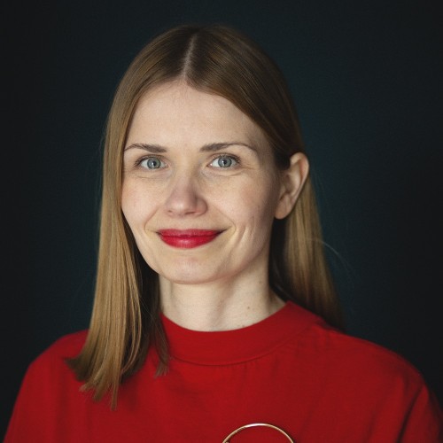Ein Porträtfoto von einer lächelnden vierzigjährigen Frau mit dunkelblonden, schulterlangen Haaren, rotem T-Shirt, rotem Lippenstift.