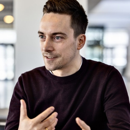 Lukas Brand, weinroter Pullover, in einer Kaffeeteria, im Gespräch 