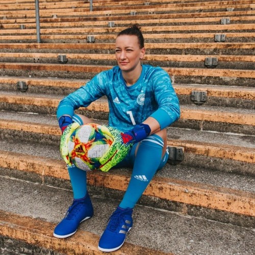 Almuth Schult sitzt in Fußball-Torwart-Outfit mit Ball in der Hand auf der einer alten Tribüne im Stadion