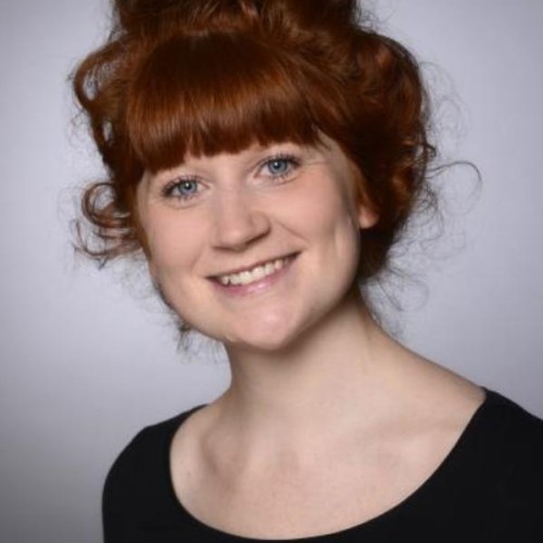 frontales Portraitfoto von Pia Zannoni. Sie hat helle Haut, rote Haare und trägt ein schwarzes, schlichtes Oberteil.