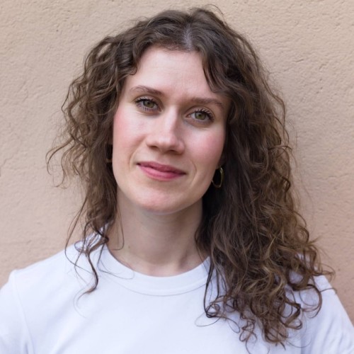 Anna-Mira Brandau steht vor einer Mauer und lächelt in die Kamera. 