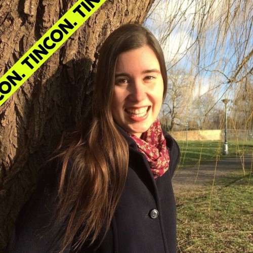 Junge, lächelnde Frau steht vor einem Baum 