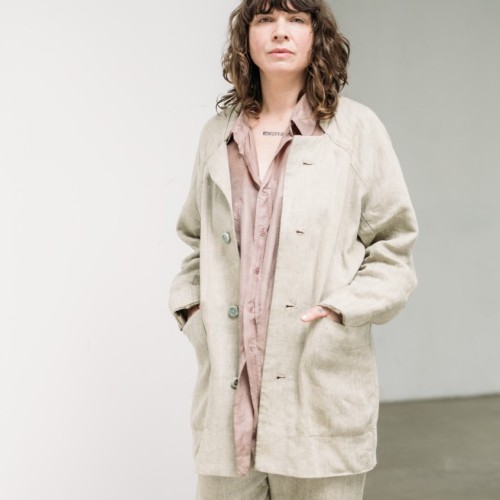 Sarah is standing looking upfront in camera, hands in pockets, earing pale green suit and rose shirt.
