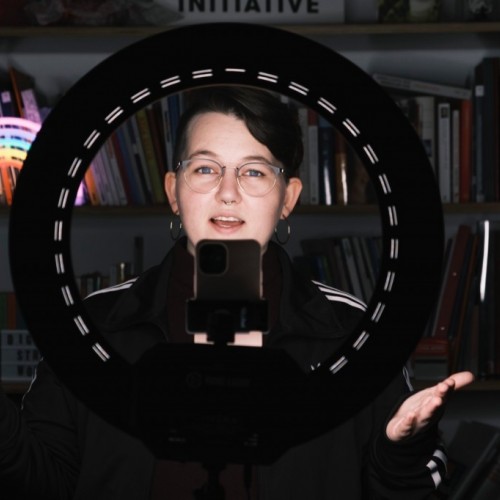 Eine Person steht hinter einem Ringlicht und spricht in eine Handykamera