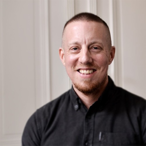 Florian Köhler lächelnd im Portrait mit schwarzem Hemd vor hellem Hintergrund