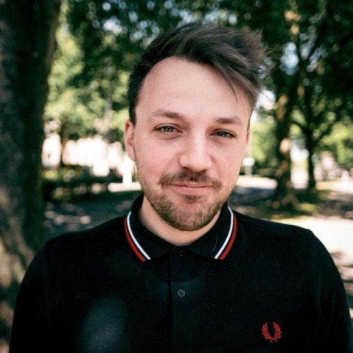 Ein Foto von Gavin Karlmeier. Einem Mann, der im schwarzen Poloshirt in einem Park steht. Sein Bild ist in die Kamera gerichtet.