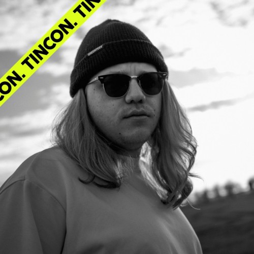 schwarz-weiß Foto von einem Mann mit langen blonden Haaren, er trägt eine Sonnenbrille, eine Mütze und ein lockeres Sweatshirt