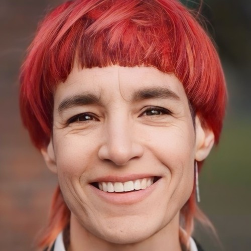 Eine non-binäre Person mit kurzen roten Haaren, die lächelt
