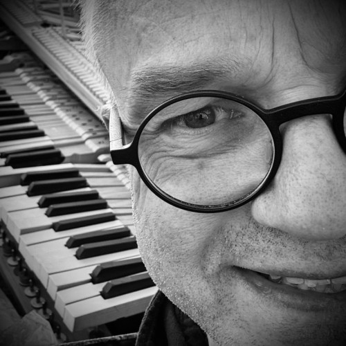 Selfi , with only half of his face, wearing glasses in front of a broken piano keyboard
