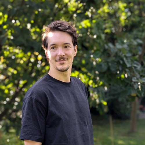 Auf dem Foto ist der Journalist Johannes Giesler zu sehen, er steht vor einem grünen Hintergrund aus Blättern.
