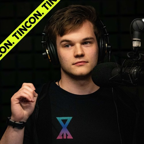 Junger Mann vor einem schwarzen Hintergrund, trägt ein schwarzes Tshirt und große Over-Ear-Kopfhörer, schaut konzentriert aus
