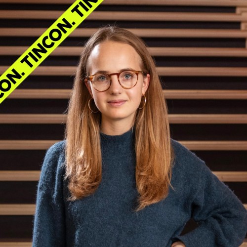 Junge Frau mit Brille und langen Haaren steht vor einer Treppe