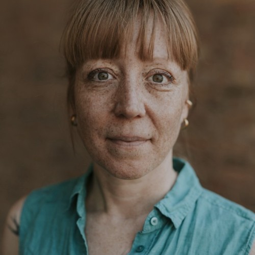 Portraitbild: Frau mit rötlichem Haar, Sommersprossen und Dutt in grüner Bluse 