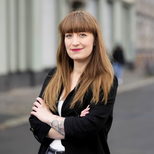 Foto von Heidi Reichinnek. Sie trägt Pony und langes Haar. Mit verschränkten Armen und leichtem Lächeln schaut sie in die Kamera