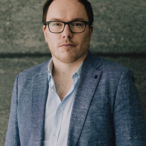 Portraitfoto von Daniel Drepper – brille, dunkle Haare – in Hemd und Sakko