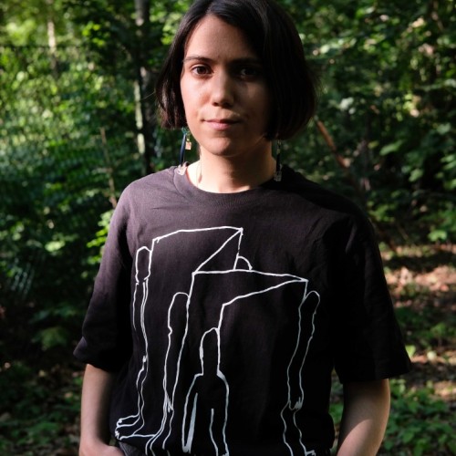 frontal image of Ipek Burçak, a light-brown skinned female person standing in the nature wearing a black T-shirt, short brown hair, showing her upper body