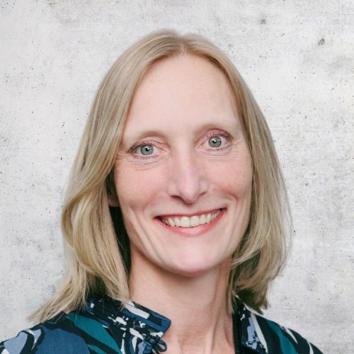 Portrait Antje Olzem. Sie hat schulterlange, blonde Haare, trägt eine gemusterte Bluse in Blau- und Grüntönen und lächelt in die Kamera.