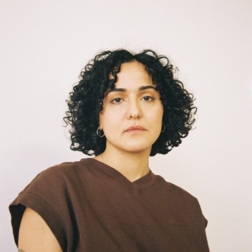 Duygu steht entschlossenen und schaut dezent melancholischen Blickes direkt in die Kamera. Seine*Ihre Schulter ist leicht weggedreht von dem*der Beobachter*in.