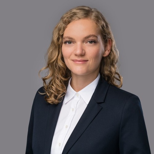 Ein Portraitfoto von Christin Schemmann, eine Frau mitte 20 mit blonden Locken. Sie trägt einen Anzug. 
