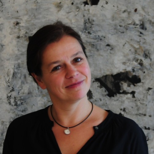Eine Frau mit schwarzer Bluse und hochgesteckten Haaren - Tanja Busse - guckt in die Kamera