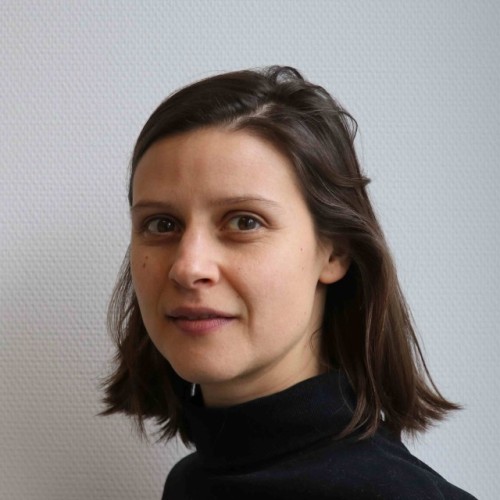 Person mit mittellangen, braunen Haaren vor weißem Hintergrund