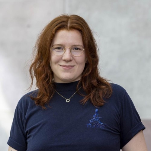 Abgebildet ist Marie Weigert, eine Person mit schulterlangen rötlichen Haaren, einer Brille und dunkelblauer Kleidung.