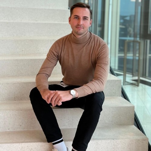 Photo of Frederik Heinz, sitting on a stairway and smiling at you