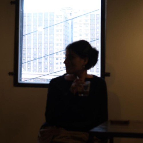 Blurred silhouette of a woman sitting, facing right, with a backlight from a large window behind her.