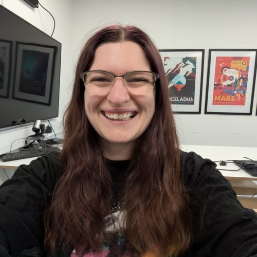 Photo of Beth smiling in her lab with space-themed posters behind her.