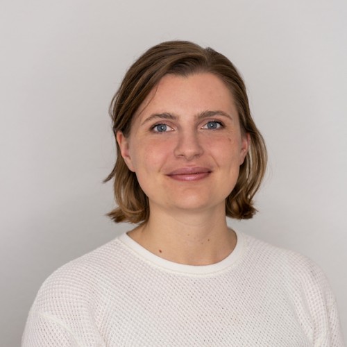 Portraitfoto vor neutralem weißen Hintergrund, Person mit blonden Haaren und weißem Pullover.