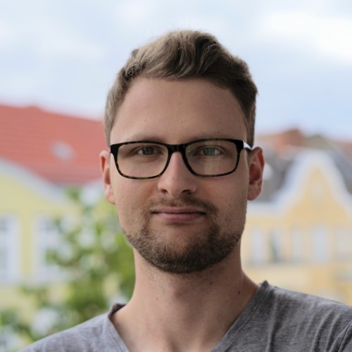 Portraitfoto von Nándor. Er hat braune, eher kurze Haare und trägt eine Brille und ein graues T-Shirt.