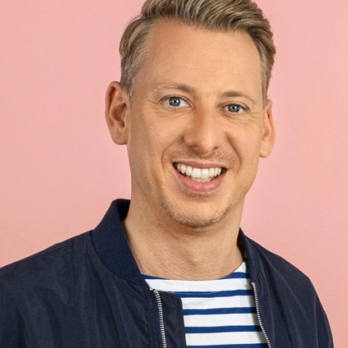 André Schünke lächelnd vor einem lachsfarbenen Hintergrund