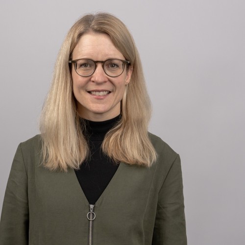 dunkelblonde lange Haare, runde hellbraune Brille, lächelnd