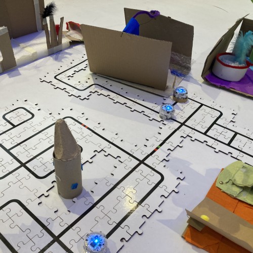 Roboter fahren auf Linien durch eine Stadt, deren Gebäude selbst gebastelt sind.