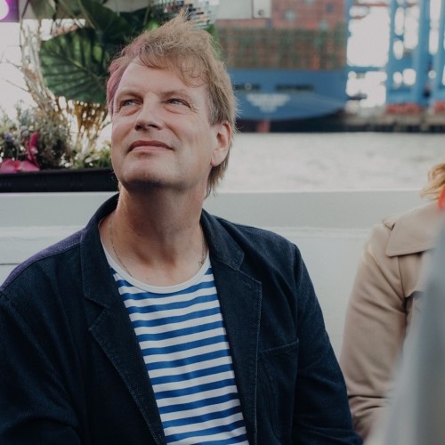 Wolfgang auf einem Boot im Hamburger Hafen in blau-weiß gestreitem Shirt und blauem Sakko.