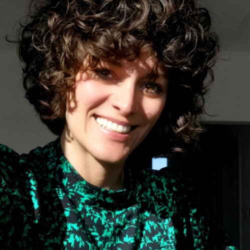 Katarina Roncevic, Mitarbeiterin des Bildungsteams von Greenpeace e.V., eine Frau mit dunklen Locken in einer grün-schwarzen Bluse, blickt lächelnd in die Kamera.