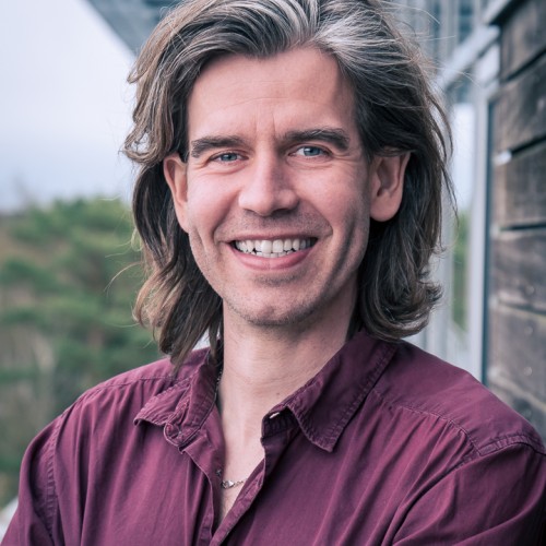 Portraitfoto eines lächelden Mannes mit langen Haaren  